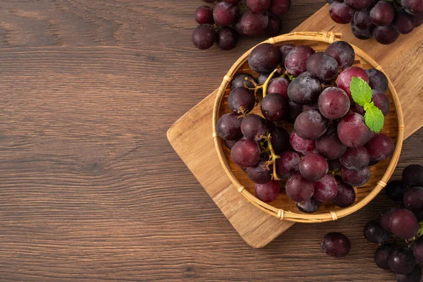 Delicious bunch of purple grapes fruit in a plate on wooden table background.