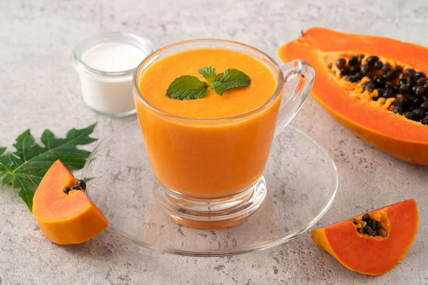Fresh delicious papaya milk smoothie in glass cup on gray table background for tropical fruit design concept.