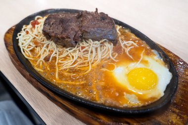 Tayvan usulü özel cızırtılı biftek, erişte, yumurta ve sos geleneksel gece pazarında sıcak demir bir tahtanın üzerinde..