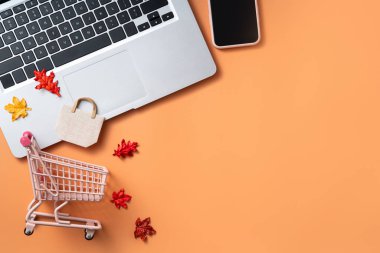 Alışveriş arabası, dizüstü bilgisayar, akıllı telefon ve akçaağaç yapraklı sonbahar çevrimiçi alışveriş tasarımı konsepti.