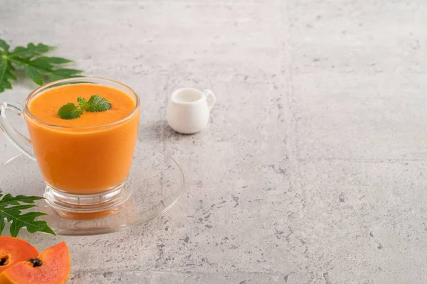 Fresh delicious papaya milk smoothie in glass cup on gray table background for tropical fruit design concept.