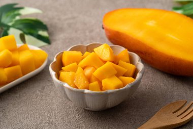 Gri masa zemininde taze doğranmış mango küpleri ve tropikal yaprak yemek için..