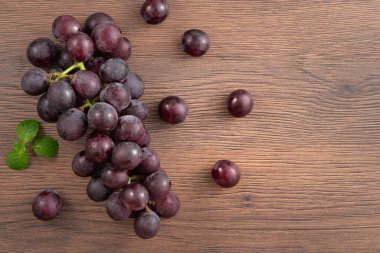 Ahşap masa arkasındaki bir tabakta lezzetli mor üzüm meyveleri..