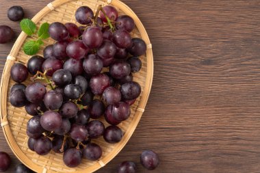 Ahşap masa arkasındaki bir tabakta lezzetli mor üzüm meyveleri..