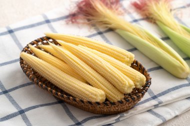 Çiğ, taze mısır kabuğunda, gri masa arkasında kırmızı ipek sepet elek tabağı..