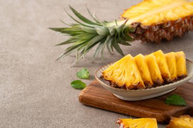 Taze dilimlenmiş ve kesilmiş ananas, gri masa arkasında tropikal meyve parçaları..