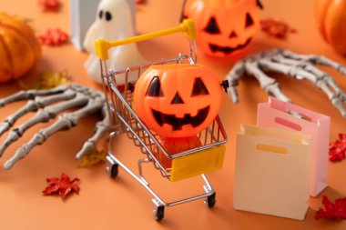 Alışveriş arabası, akçaağaç yaprakları ve turuncu masa zemininde balkabağı olan Cadılar Bayramı sonbahar alışveriş tasarımı konsepti.