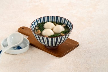 Eating big tangyuan yuanxiao, tang yuan, glutinous rice dumpling balls, with savory vegetable soup in a bowl for Winter solstice festival. clipart