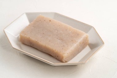 Japonya 'da Konnyaku olarak da adlandırılan beyaz masa arka planındaki bir tabakta kare şeklinde ham konjac.