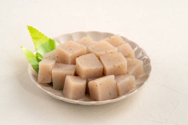 Japonya 'da Konnyaku olarak da adlandırılan beyaz masa arka planındaki bir tabakta kare şeklinde ham konjac.