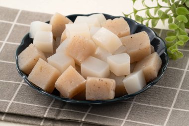 Japonya 'da Konnyaku olarak da adlandırılan beyaz masa arka planındaki bir tabakta kare şeklinde ham konjac.