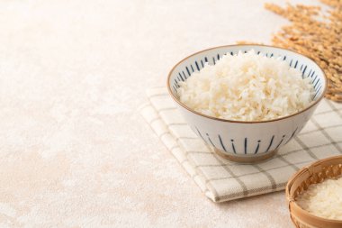 Bir kase taze pişmiş beyaz pirinç, yumuşak, kabarık ve beyaz masa arkasında hafifçe parıltılı..