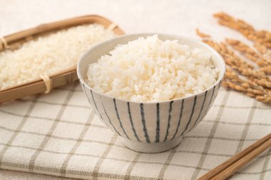 Bir kase taze pişmiş beyaz pirinç, yumuşak, kabarık ve beyaz masa arkasında hafifçe parıltılı..