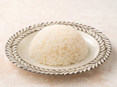 Bir kase taze pişmiş beyaz pirinç, yumuşak, kabarık ve beyaz masa arkasında hafifçe parıltılı..