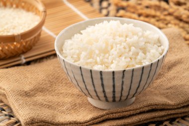 Bir kase taze pişmiş beyaz pirinç, yumuşak, kabarık ve beyaz masa arkasında hafifçe parıltılı..