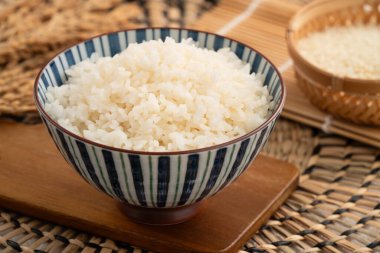 Bir kase taze pişmiş beyaz pirinç, yumuşak, kabarık ve beyaz masa arkasında hafifçe parıltılı..