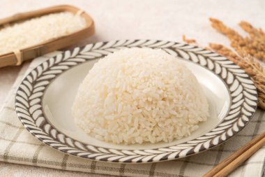 Bir kase taze pişmiş beyaz pirinç, yumuşak, kabarık ve beyaz masa arkasında hafifçe parıltılı..