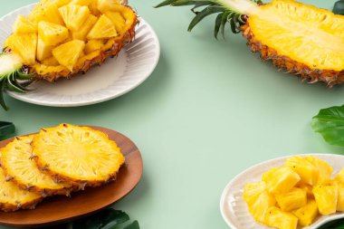 Arkaplanda tropik yapraklar olan yarım bir ananas kasesine yerleştirilmiş sulu ananas parçaları..