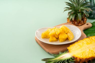 Arkaplanda tropik yapraklar olan yarım bir ananas kasesine yerleştirilmiş sulu ananas parçaları..