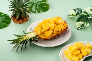 Arkaplanda tropik yapraklar olan yarım bir ananas kasesine yerleştirilmiş sulu ananas parçaları..