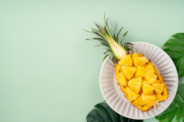 Arkaplanda tropik yapraklar olan yarım bir ananas kasesine yerleştirilmiş sulu ananas parçaları..