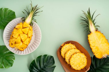 Arkaplanda tropik yapraklar olan yarım bir ananas kasesine yerleştirilmiş sulu ananas parçaları..