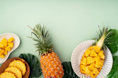 Arkaplanda tropik yapraklar olan yarım bir ananas kasesine yerleştirilmiş sulu ananas parçaları..