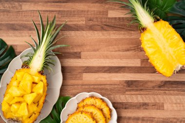 Arkaplanda tropik yapraklar olan yarım bir ananas kasesine yerleştirilmiş sulu ananas parçaları..