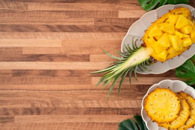 Arkaplanda tropik yapraklar olan yarım bir ananas kasesine yerleştirilmiş sulu ananas parçaları..