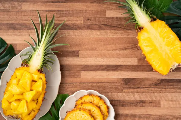 Arkaplanda tropik yapraklar olan yarım bir ananas kasesine yerleştirilmiş sulu ananas parçaları..