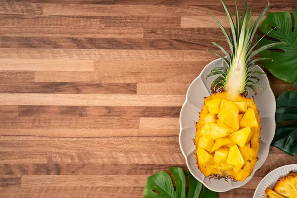 Arkaplanda tropik yapraklar olan yarım bir ananas kasesine yerleştirilmiş sulu ananas parçaları..