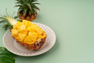 Arkaplanda tropik yapraklar olan yarım bir ananas kasesine yerleştirilmiş sulu ananas parçaları..