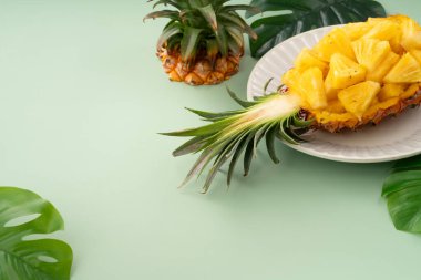 Arkaplanda tropik yapraklar olan yarım bir ananas kasesine yerleştirilmiş sulu ananas parçaları..