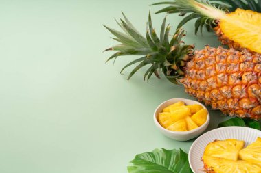 Arkaplanda tropik yapraklar olan yarım bir ananas kasesine yerleştirilmiş sulu ananas parçaları..