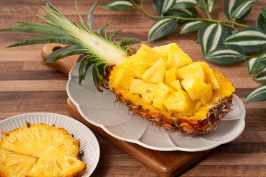 Arkaplanda tropik yapraklar olan yarım bir ananas kasesine yerleştirilmiş sulu ananas parçaları..