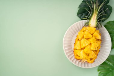 Arkaplanda tropik yapraklar olan yarım bir ananas kasesine yerleştirilmiş sulu ananas parçaları..