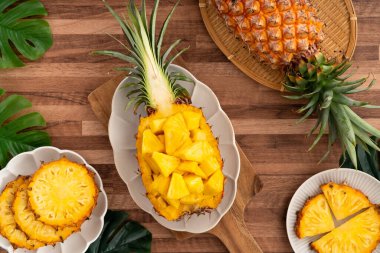 Arkaplanda tropik yapraklar olan yarım bir ananas kasesine yerleştirilmiş sulu ananas parçaları..