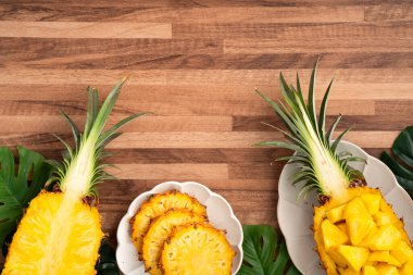 Arkaplanda tropik yapraklar olan yarım bir ananas kasesine yerleştirilmiş sulu ananas parçaları..