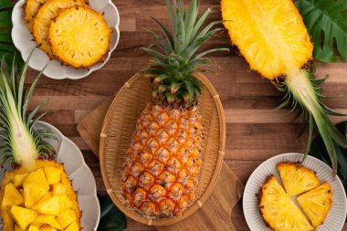Arkaplanda tropik yapraklar olan yarım bir ananas kasesine yerleştirilmiş sulu ananas parçaları..
