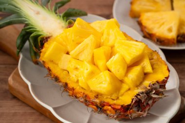 Arkaplanda tropik yapraklar olan yarım bir ananas kasesine yerleştirilmiş sulu ananas parçaları..