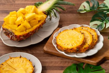 Arkaplanda tropik yapraklar olan yarım bir ananas kasesine yerleştirilmiş sulu ananas parçaları..