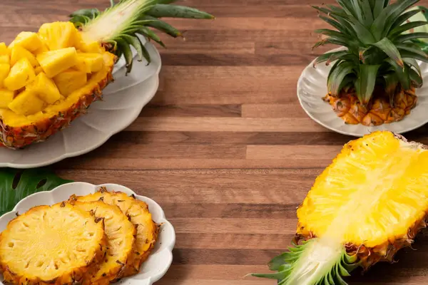 Arkaplanda tropik yapraklar olan yarım bir ananas kasesine yerleştirilmiş sulu ananas parçaları..