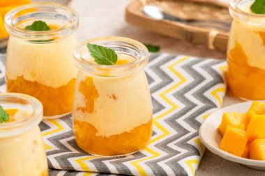 Cam bardaklarda servis edilen, nane yapraklarıyla kaplı taze mango mus tatlısı, yaz için mükemmel..