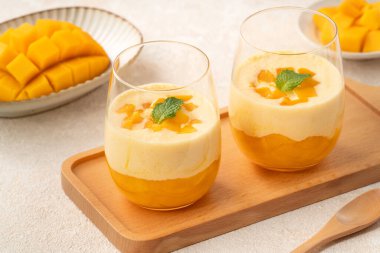 Cam bardaklarda servis edilen, nane yapraklarıyla kaplı taze mango mus tatlısı, yaz için mükemmel..