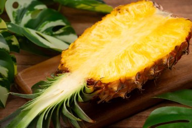 Arkaplanda tropik yapraklar olan yarım bir ananas kasesine yerleştirilmiş sulu ananas parçaları..