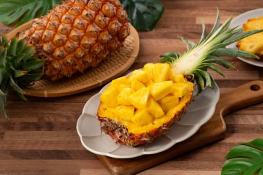 Arkaplanda tropik yapraklar olan yarım bir ananas kasesine yerleştirilmiş sulu ananas parçaları..