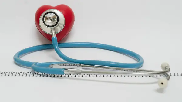 Stetoskop kırmızı kalp şeklindeki nesneye dayanır, sağlık ve kardiyolojiyi sembolize eder. Görüntü, tıbbi bakım ve kalp sağlığı bilincini iletir