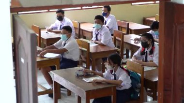 BALI, INDONESIA-5 OCT 2021: Endonezya ortaokulundaki sınıf atmosferi yeni normalliği öğrenirken. Öğrenciler sınıfta çalışırken sağlık maskesi takıyor.
