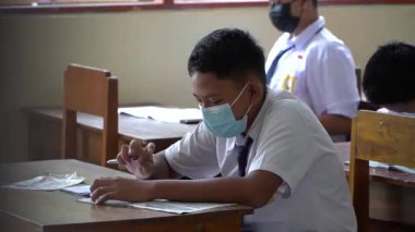 BALI, INDONESIA-5 OCT 2021: Endonezya ortaokulundaki sınıf atmosferi yeni normalliği öğrenirken. Öğrenciler sınıfta çalışırken sağlık maskesi takıyor.