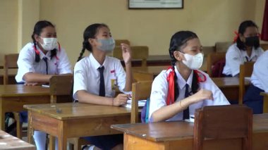 BALI, INDONESIA-5 OCT 2021: Endonezya ortaokulundaki sınıf atmosferi yeni normalliği öğrenirken. Öğrenciler sınıfta çalışırken sağlık maskesi takıyor.